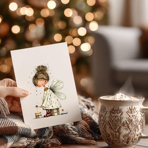 May include: A greeting card featuring a whimsical illustration of a fairy holding a candle. The fairy wears a white dress with star accents and has delicate wings. A steaming mug of a beverage sits nearby, with a cozy blanket in the foreground.
