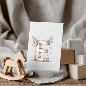 May include: A watercolor illustration of the letter "E" adorned with butterfly wings and floral accents. The letter is on a white card, with a wooden rocking horse and blocks in the foreground. Soft pastel colors are used.
