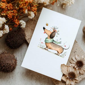 May include: A watercolour illustration of a dachshund wearing a green scarf and a floral crown. A yellow butterfly hovers near the dog's nose. The dog is on a white card, surrounded by dried flowers and decorative elements.