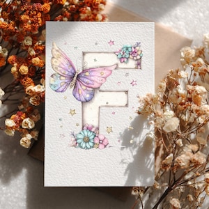 May include: A watercolor greeting card featuring a butterfly with purple, pink, and blue wings. The butterfly is positioned on a letter "F" decorated with flowers and stars. The card is on a neutral background with dried flowers.