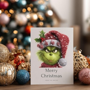 Peut inclure: Carte de No&euml;l avec un personnage vert portant un bonnet de P&egrave;re No&euml;l rouge et des feuilles de houx. La carte indique "Joyeux No&euml;l" avec un nom de famille. En arri&egrave;re-plan, des lumi&egrave;res et des boules de No&euml;l floues.
