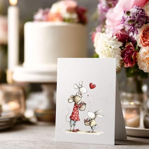 May include: A greeting card featuring an illustration of two mice holding baskets, with a red heart above them. The mouse on the left wears a red dress with white polka dots. A white cake and flowers are in the background.