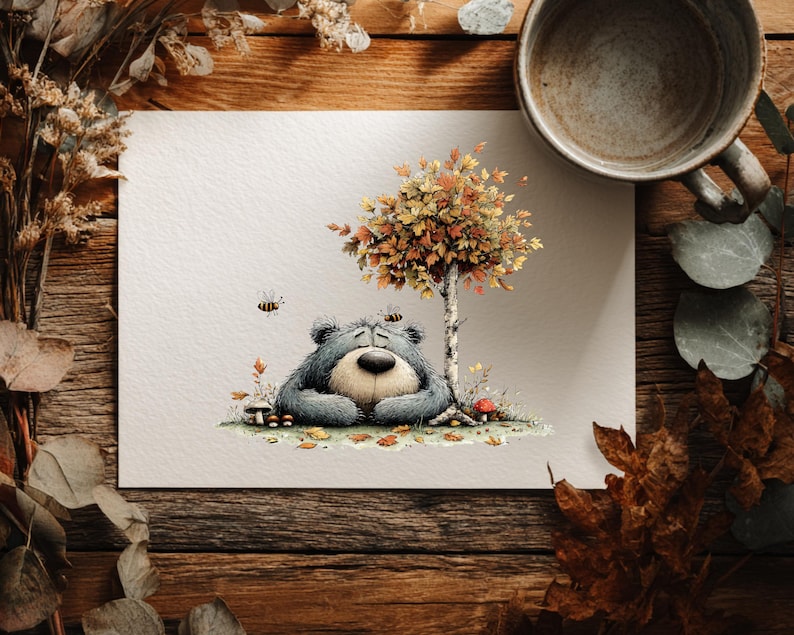 May include: A watercolour illustration of a bear resting under a tree with autumn leaves. The bear is grey with a tan snout and is surrounded by mushrooms, bees, and fallen leaves. The artwork is on white paper, set on a wooden surface.