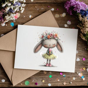 May include: A greeting card featuring a watercolor illustration of a bunny wearing a flower crown and tutu, holding an ice cream cone. The card is on a wooden surface with a brown envelope and floral arrangements.