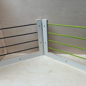 May include: Two white wooden climbing frames with horizontal bars. One frame has black bars, the other has bright green bars. The frames are set against a light wood background, suggesting a children's play area.