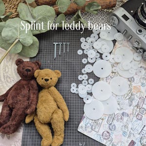 May include: Two teddy bears, one brown and one tan, are positioned near a collection of white splints and fasteners. The text "Splint for teddy bears" is written in a script font above the bears.