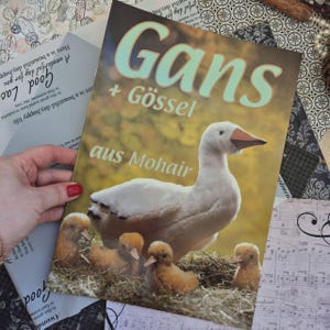 Op de afbeelding: Een rechthoekige boekomslag met de titel Gans + GÖSSEL aus Mohair, met een grote witte gans die over vier kleine, donzige, lichtbruine gansjes in een strooien nest staat tegen een wazige, warmgekleurde natuurlijke achtergrond.