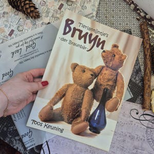 May include: A book titled Tierlantijntje's Bruyn -der Braunbär- by Toos Keuning featuring a cover illustration of two brown teddy bears and a small dark blue glass bottle. The book cover has a light cream background with dark brown text.