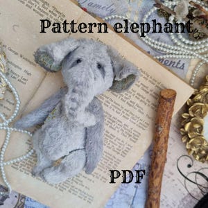 Puede incluir: Un juguete de peluche de elefante gris con una trompa larga y orejas grandes. El juguete está sentado en un libro con la palabra "PDF" impresa en la página. El libro está rodeado por un collar de perlas y un palo de madera.
