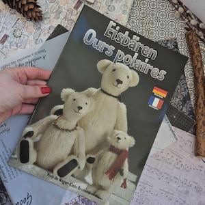 Op de afbeelding: Een boek getiteld Eisbären Ours polaires met drie crèmekleurige teddyberen op de kaft. De beren hebben donkere neuzen en ogen, waarbij er één een rode sjaal draagt en een andere een groene kralenketting. Auteur is Riny de Weger-Klein Bruinink.