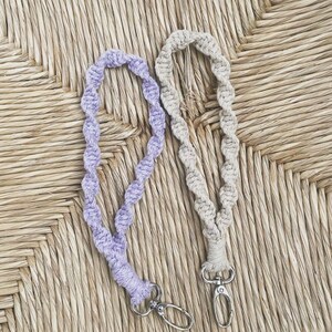 Peut inclure: Deux porte-cl&eacute;s en crochet avec des clips pivotants argent&eacute;s. Un porte-cl&eacute;s est lavande et l'autre beige. Les porte-cl&eacute;s sont pr&eacute;sent&eacute;s sur une surface tiss&eacute;e.