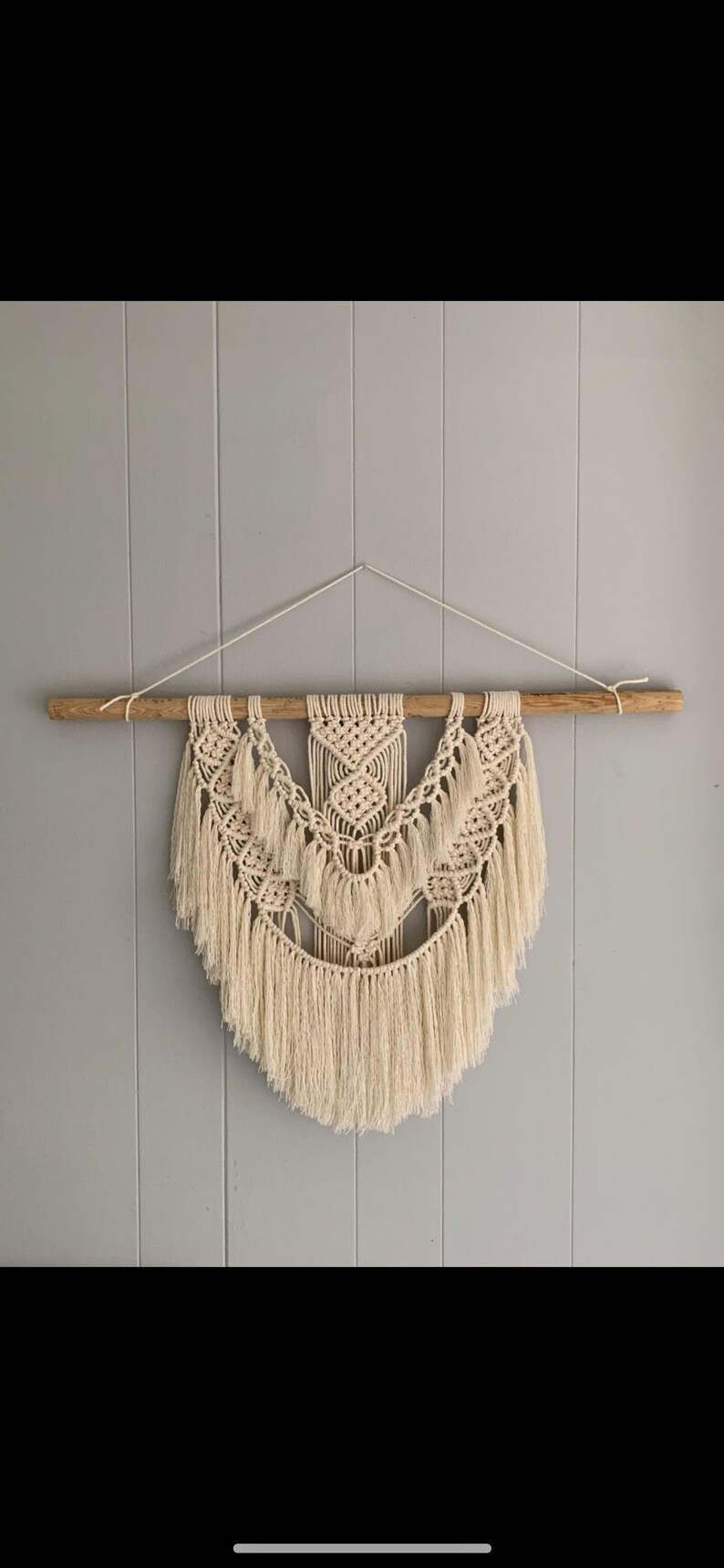 Peut inclure: Une suspension murale en macram&eacute; beige avec une tringle en bois en haut. La suspension pr&eacute;sente un motif g&eacute;om&eacute;trique avec des d&eacute;tails en franges.