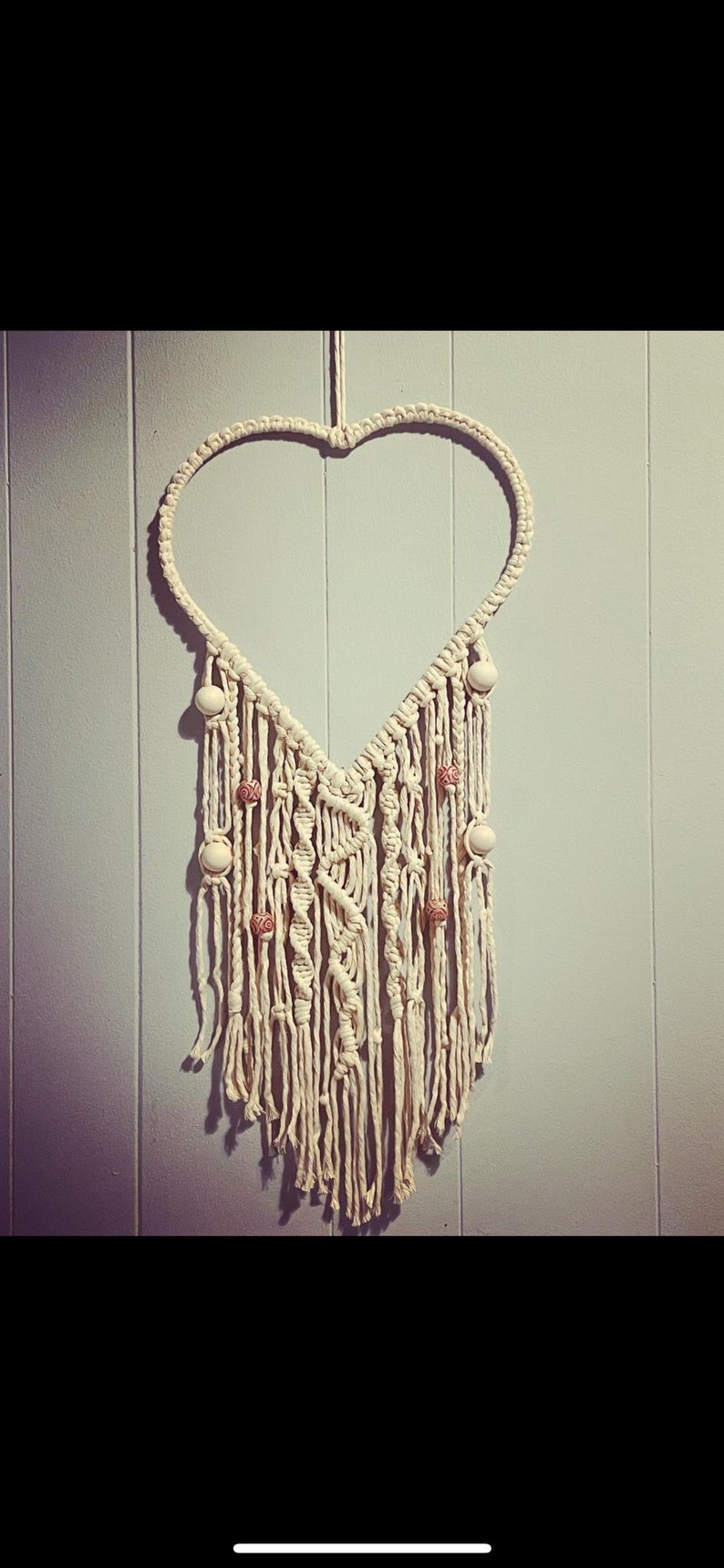 Peut inclure: Une suspension murale en macram&eacute; en forme de c&oelig;ur blanche avec des perles en bois. Le macram&eacute; est r&eacute;alis&eacute; avec un cordon blanc &eacute;pais et pr&eacute;sente une frange en bas.