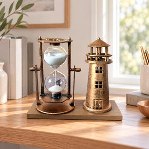 Könnte beinhalten: Ein dekoratives Tischobjekt mit einer rotierenden Sanduhr aus Glas, gefüllt mit weißem Sand, montiert in einem bronzefarbenen Metallrahmen, neben einer passenden bronzefarbenen Leuchtturmfigur auf einem rechteckigen Sockel mit Ziegelmuster.