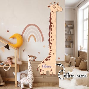 May include: A giraffe-shaped wooden growth chart featuring a light tan body with dark brown spots, a long neck, and a measurement scale from 2 to 6. The name Oliver is printed in purple script on the base, with an arrow pointing to the custom name.