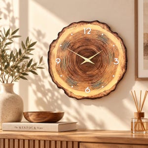 May include: A round wall clock featuring a natural wood slice design with visible tree rings in shades of brown and tan. The clock face includes white numerals at the 12, 3, 6, and 9 o'clock positions, with simple white dots for other hours and thin gold-colored hands.