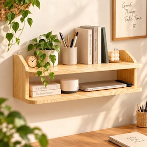 Può includere: Una mensola da parete a due livelli in legno chiaro con venature visibili. Il ripiano superiore ospita una pianta verde in vaso, un orologio rotondo in legno, un portapenne cilindrico con penne e tre libri. Il ripiano inferiore ospita due libri, un dispositivo bianco e un computer portatile.