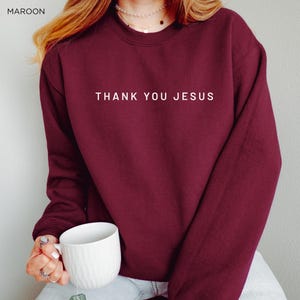 Peut inclure: Un sweat-shirt bordeaux avec le texte "THANK YOU JESUS" imprim&eacute; en blanc sur le devant.