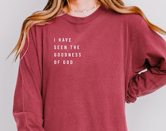 Peut inclure: Un t-shirt à manches longues bordeaux avec le texte blanc "I HAVE SEEN THE GOODNESS OF GOD". Le t-shirt a un col rond et une coupe ample. Le tissu semble doux et confortable.