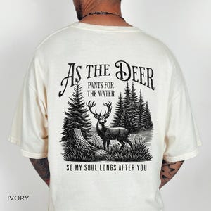 May include: Ivory t-shirt with a black graphic print of a deer in a forest with the text "As the Deer, Pants for the Water, So my soul longs after you".