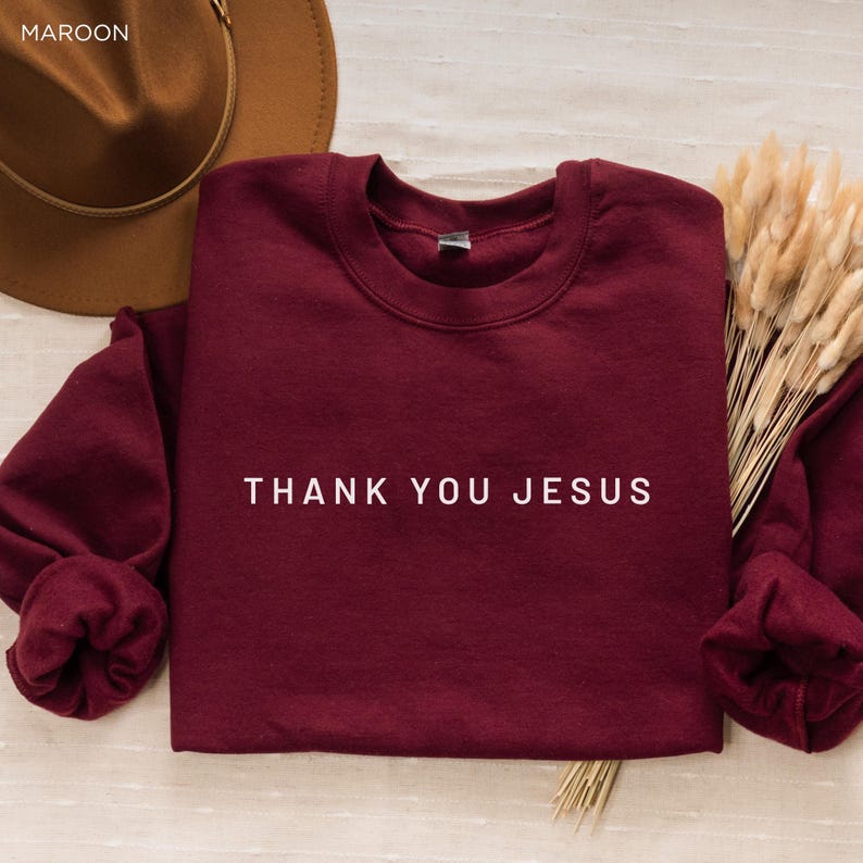 Peut inclure: Un sweat-shirt bordeaux avec le texte "THANK YOU JESUS" en lettres blanches.