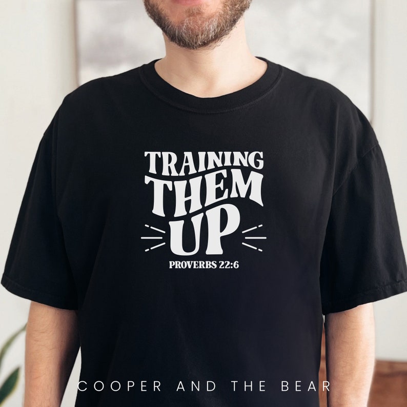May include: Black t-shirt with white text that reads "Training Them Up" and "Proverbs 22:6".