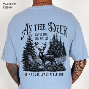 May include: A light blue t-shirt with a black graphic print of a deer in a forest. The text "As the Deer" is above the deer and the text "Pants for the Water" is below the deer. The text "So my soul longs after you" is at the bottom of the graphic.