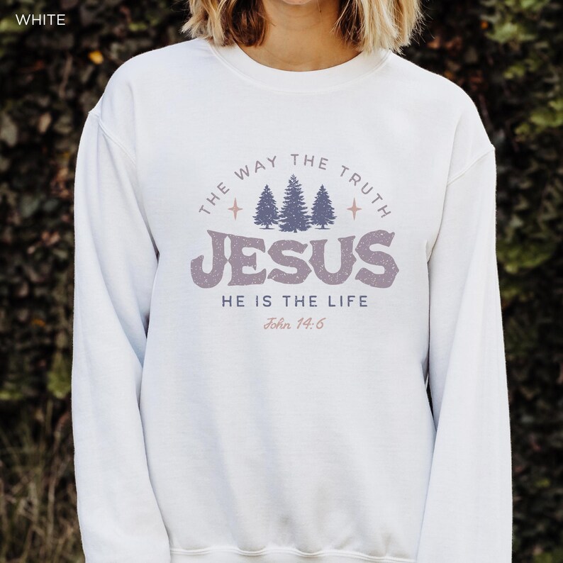 May include: White sweatshirt with the text "THE WAY THE TRUTH JESUS HE IS THE LIFE John 14:6" in a circular design. The design includes three stylized pine trees and star accents, in shades of purple and gray.