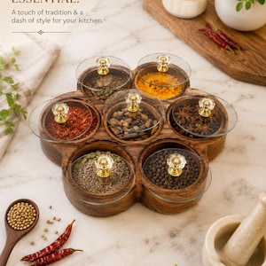 Peut inclure: Une boîte à épices en bois dotée de sept compartiments circulaires, chacun muni d'un couvercle en verre transparent et d'un bouton doré avec un accent en cristal. La boîte contient diverses épices, dont du poivre, du piment et de l'anis étoilé.