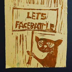 Peut inclure: Un panneau en papier brun avec une illustration dessinée à la main d'un chat tenant un panneau qui dit "Let's Facebattle".