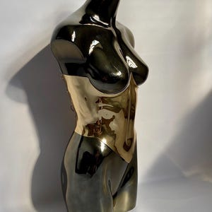 Puede incluir: Escultura met&aacute;lica de un torso, con un dise&ntilde;o bicolor. La parte superior es negra brillante, que transiciona a una secci&oacute;n media dorada. La escultura es una representaci&oacute;n estilizada de la forma humana, con superficies lisas y reflectantes.