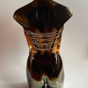 Puede incluir: Escultura decorativa de torso con acabado marr&oacute;n oscuro brillante. La escultura presenta un dise&ntilde;o tipo cors&eacute; en la parte posterior con cordones plateados. La parte inferior de la escultura tiene un acabado gris met&aacute;lico.