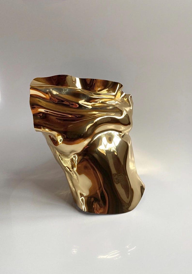Puede incluir: Una escultura abstracta dorada con un dise&ntilde;o ondulado y fluido. La superficie met&aacute;lica refleja la luz, creando reflejos y sombras. La forma es org&aacute;nica y parece ser una representaci&oacute;n estilizada de un torso.