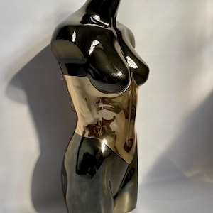 May include: A metallic sculpture of a torso, featuring a two-tone design. The upper portion is a glossy black, transitioning to a gold-colored midsection. The sculpture is a stylized representation of the human form, with smooth, reflective surfaces.
