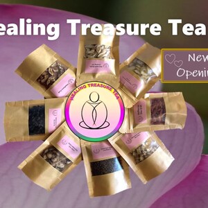 Op de afbeelding: Een assortiment theemengsels in kleine bruine papieren zakjes, gerangschikt in een cirkel. De zakjes zijn gelabeld met "Healing Treasure Tea" en hebben een logo van een persoon die in lotushouding zit. De tekst "New Opening!" staat in een roze hartvormige doos.