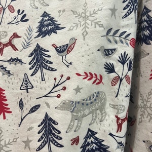 May include: White fabric with a repeating pattern of blue and red stylized trees, bears, birds, and snowflakes. The fabric has a subtle speckled texture.