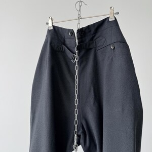 May include: Dark gray high-waisted pants hanging from a metal hanger. The pants have a button closure, belt loops, and a silver chain detail running down the front. The fabric appears to be a woven material.
