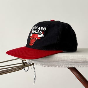 May include: Black and red baseball cap with the Chicago Bulls logo and a red brim.
