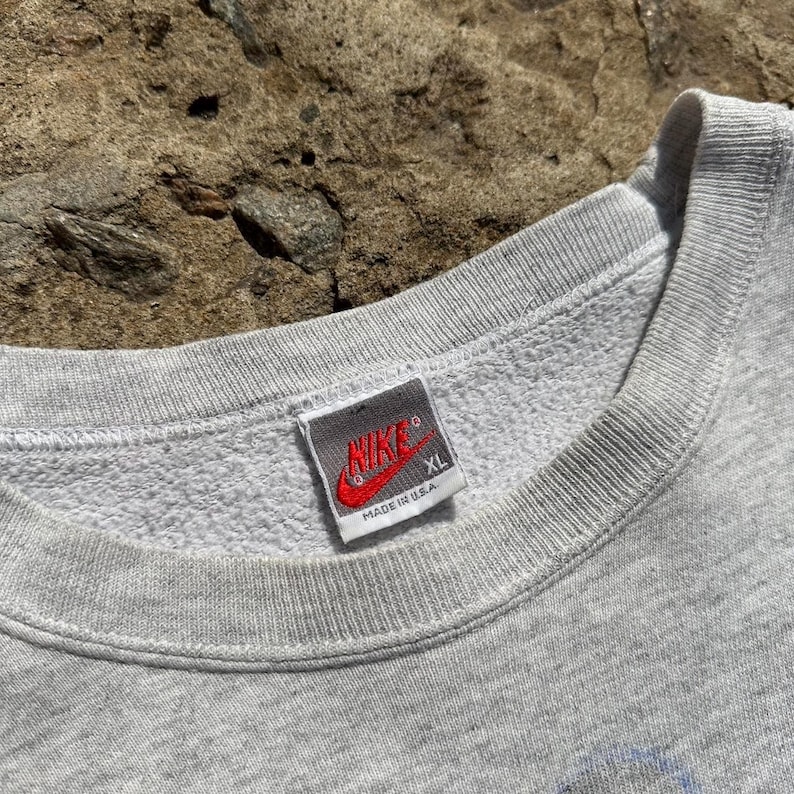Puede incluir: Sudadera gris con un logotipo de Nike y una etiqueta "Made in U.S.A.". La etiqueta tambi&eacute;n dice "XL".