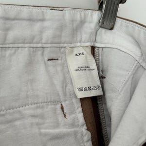 May include: A brown and white pair of pants with a white label that says "A.P.C. TISSU / FABRIC 100% COTTON / COTON" and has care instructions.