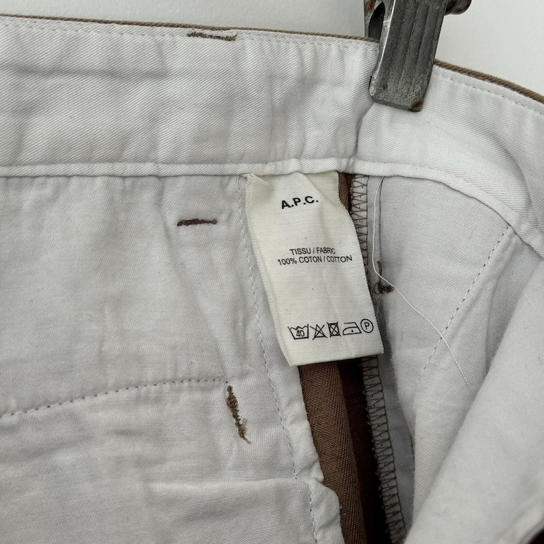 May include: A brown and white pair of pants with a white label that says "A.P.C. TISSU / FABRIC 100% COTTON / COTON" and has care instructions.