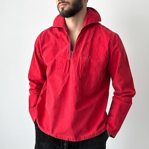 May include: A bright red long-sleeve shirt with a wide collar and a half-zip neckline. The shirt has a relaxed fit and a small pocket on the chest. The sleeves are long and the fabric appears to be a soft, textured material.