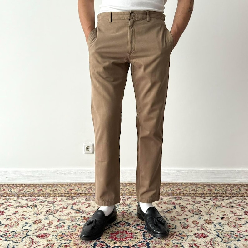May include: A pair of brown chino pants with a straight leg fit. The pants have a belt loop waistband and front pockets.