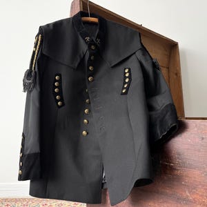 May include: A black military-style jacket with gold buttons and black velvet trim on the sleeves and collar.