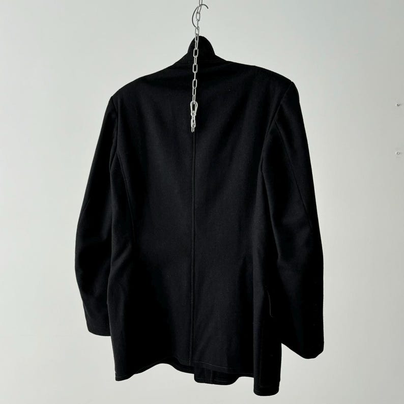 Puede incluir: Una chaqueta negra de traje con un solo bot&oacute;n de cierre y mangas largas. La chaqueta est&aacute; colgada de una cadena plateada.