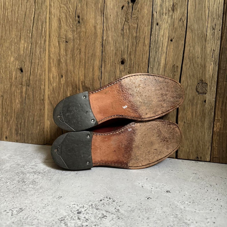 May include: The bottom of a pair of brown leather shoes with a black rubber sole. The shoes are size 3.