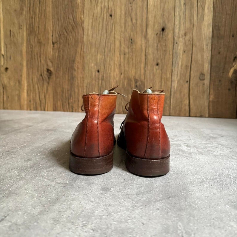 May include: A pair of brown leather ankle boots with laces. The boots have a two-tone color scheme, with a lighter brown shade on the top of the boot and a darker brown shade on the bottom.