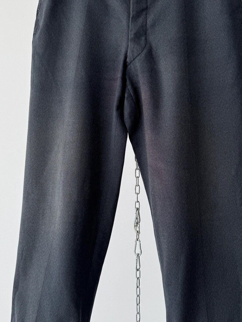 May include: Close-up of black dress pants with a straight leg design. The pants are made of a smooth fabric and have a classic, tailored look. A silver chain hangs from the pants.