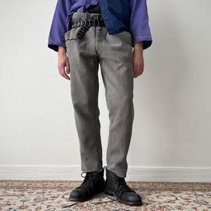 Può includere: Una persona indossa un top viola e blu navy e pantaloni grigi. La persona indossa anche una cintura nera e stivali neri. L'outfit è casual ed elegante.