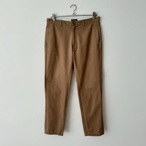 May include: Brown cotton pants with a straight leg fit. The pants have a zipper fly and belt loops.
